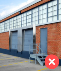 Brick wall with windows across top and two cargo blue doors next to a blue door and stairs